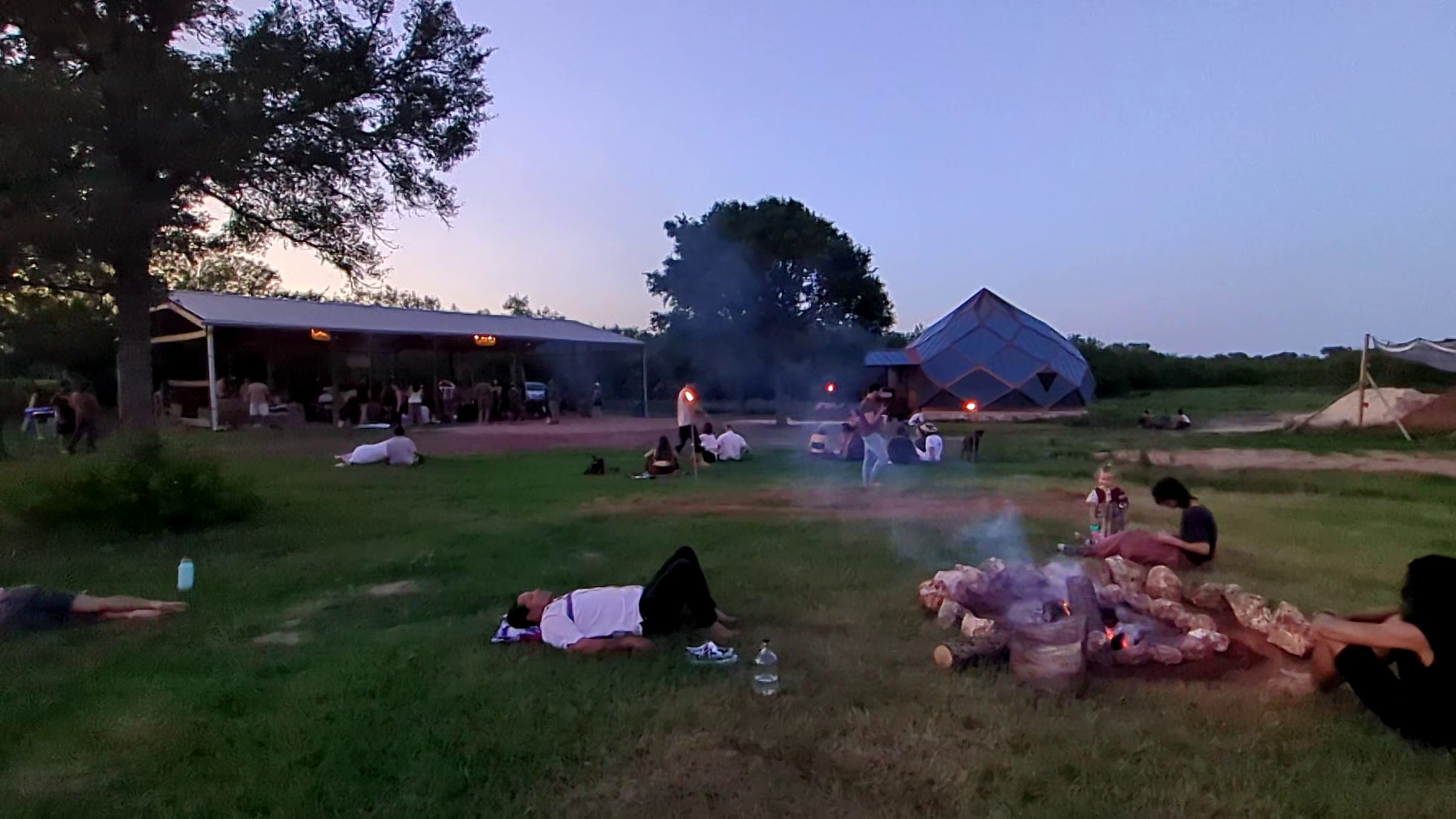 Campfire at dusk by the covered pavilion and geodesic dome